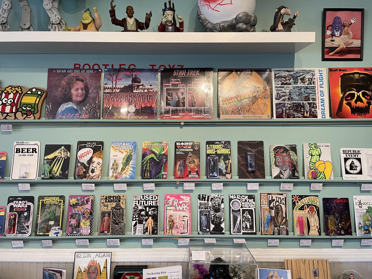 Image is of rare and eclectic figurines and their packaging lining bookshelves.