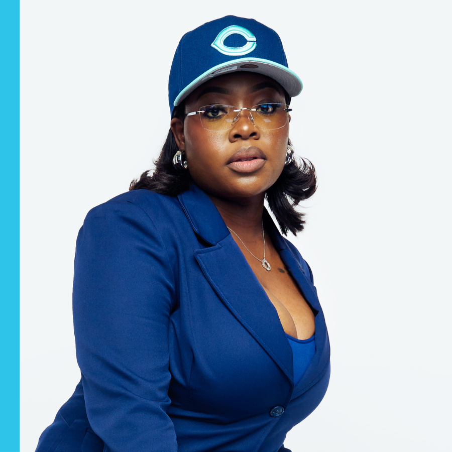 A woman in a blue blazer and baseball cap poses against a plain white background.