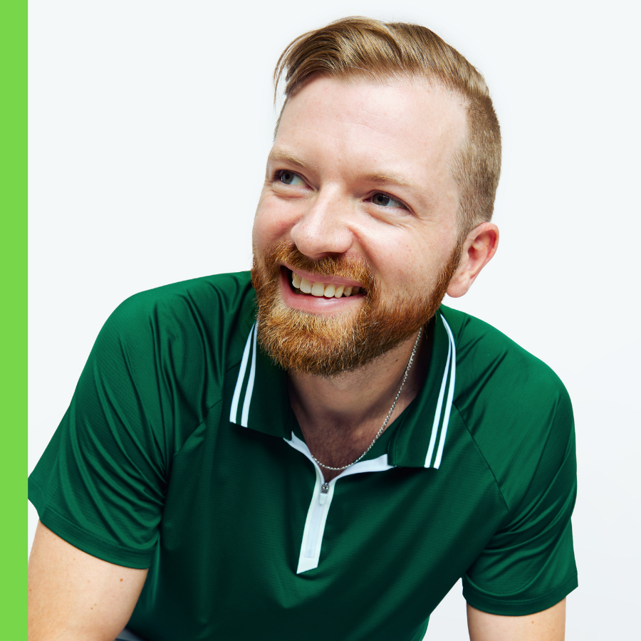 A smiling man with a beard and short hair, wearing a green polo shirt, is captured against a plain white background.