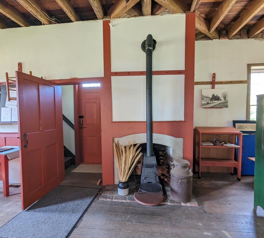 A black iron stove in front of a fireplace in the center of the photo. To the left is a door and to the right are shelves.