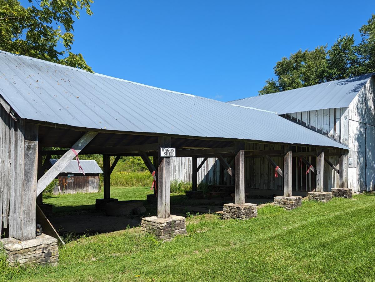 Image is of a barn on the far right and an open air garage structure with 4 openings.