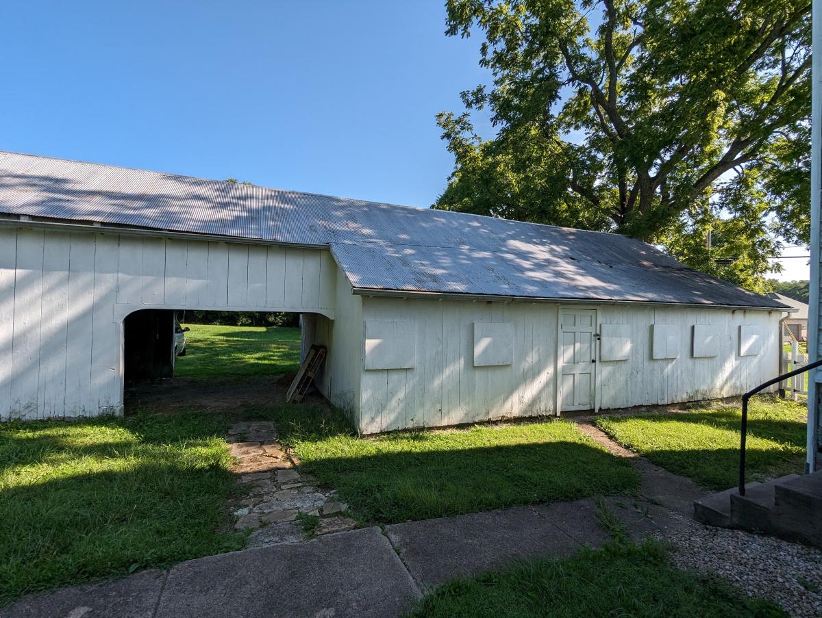 Image is of a one story barn structure with a pass through on the left.