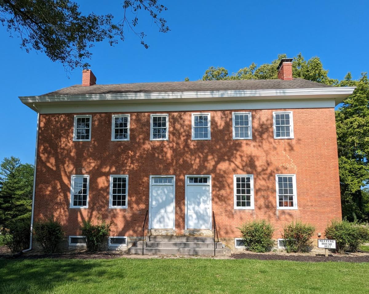 Image is of the brick Meeting House which is made from red brick, is two stories and has two white front doors next to each other in the center.