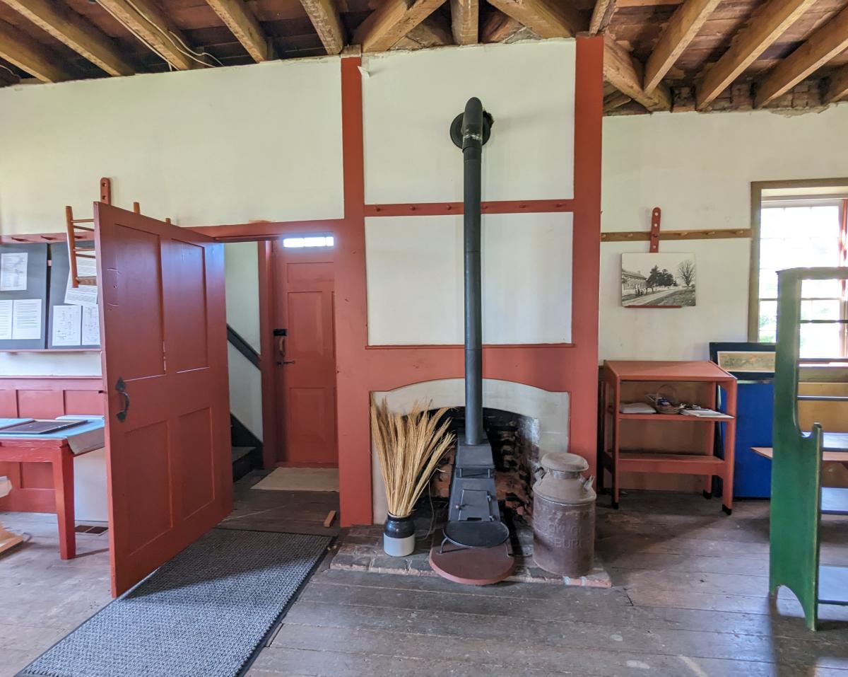 A black iron stove in front of a fireplace in the center of the photo. To the left is a door and to the right are shelves.