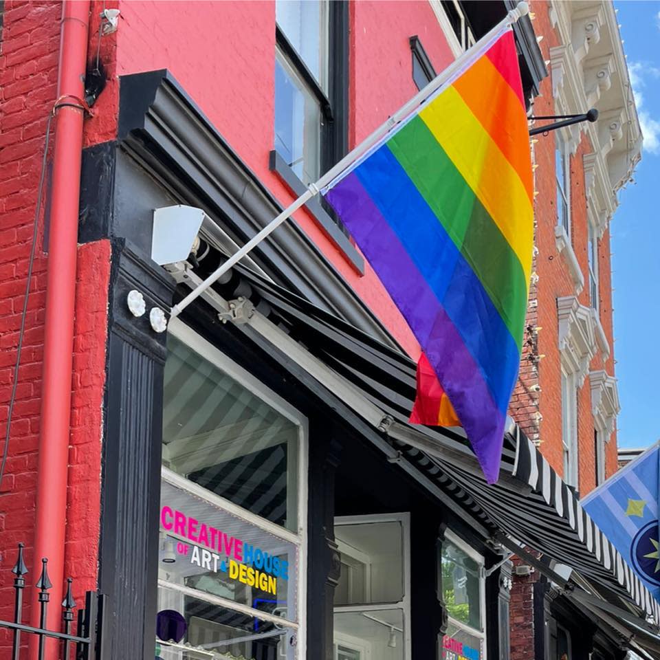 Image is of a painted red, brick building with a rainbow flag flying and the words "Creative House of Art and Design" painted in the window.
