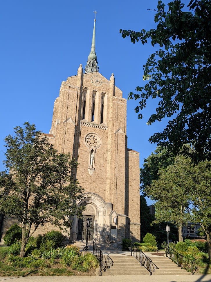 Image is of the front of St. Stephen Church with the stairs leading up to the door in the day time.