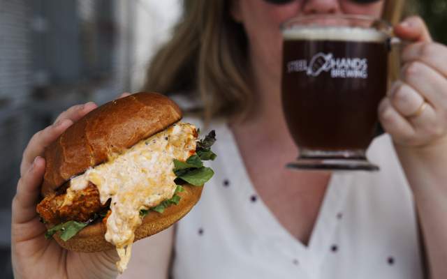 Woman holding chicken sandwich and drinking a beer
