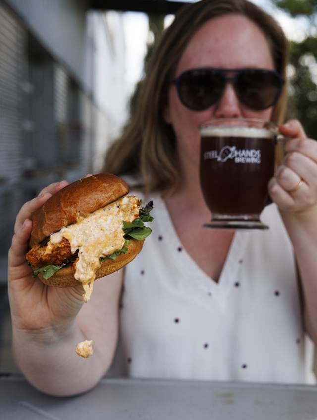 Woman holding chicken sandwich and drinking a beer