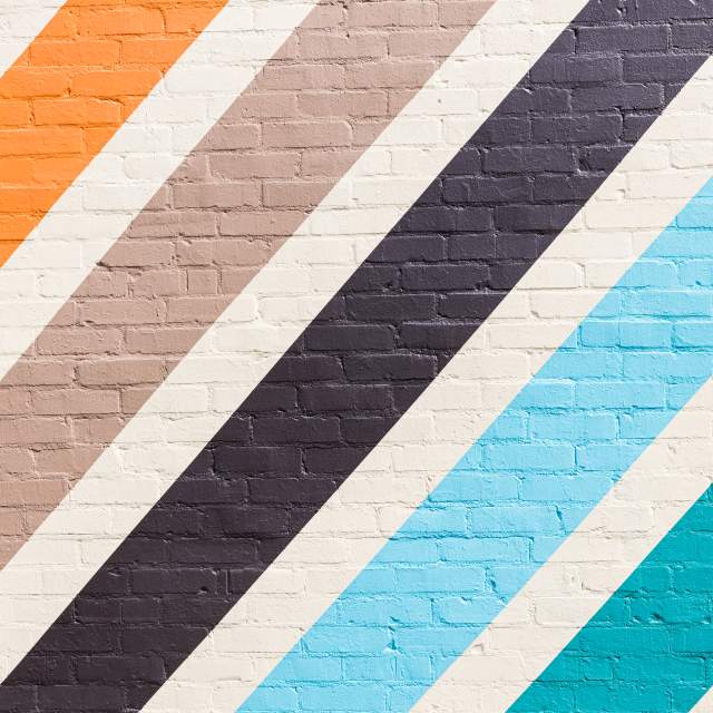 A mural on a brick wall that is painted with backslashed stripes of various colors.