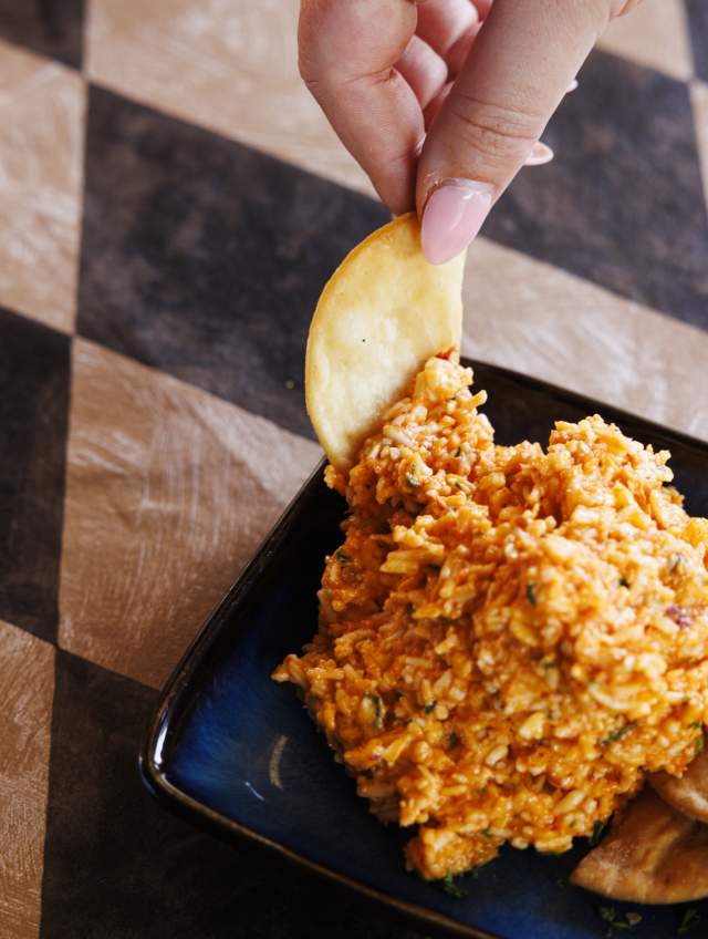 Overhead photo of pimento cheese and chips with hand holding a chip