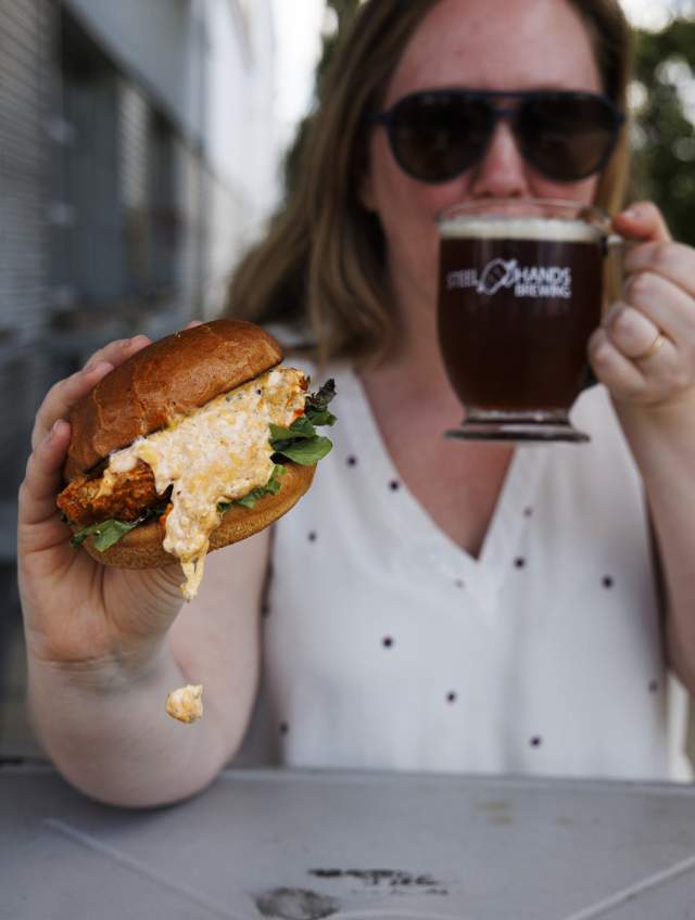 Woman holding chicken sandwich and drinking a beer
