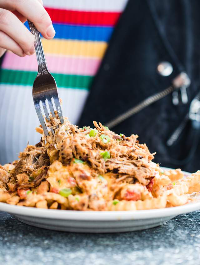 Person eating fries topped with bbq and pimento cheese