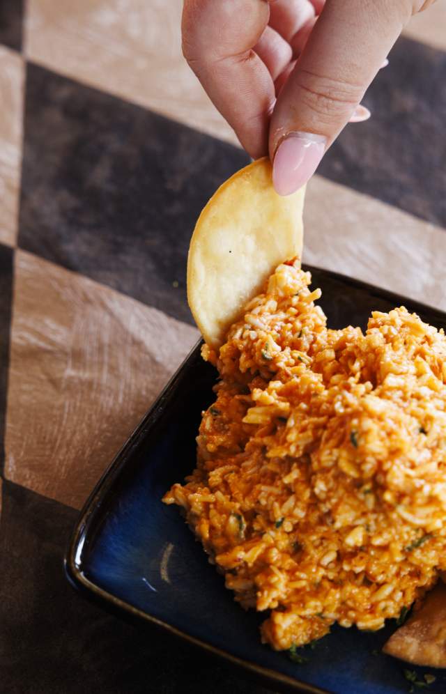 Overhead photo of pimento cheese and chips with hand holding a chip