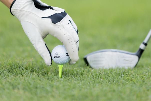 A close up photo of someone placing a golf ball on a tee stuck in the ground.