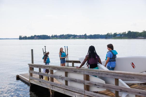 Four people stand on a dock with paddle boards at Lake Murray
