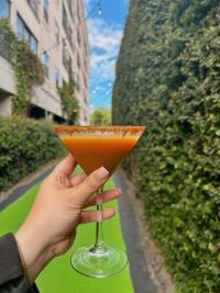 An orange, pumpkin martini head in a woman's hand with green plants in the background