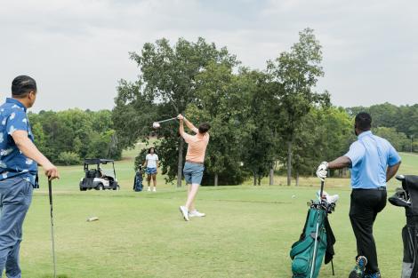 A person tees off on a golf tee pad while two others stand to the side and observe.