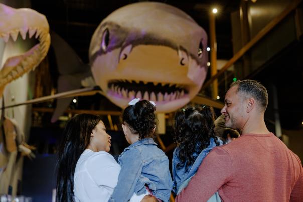 Parents holding daughters looking at shark statue