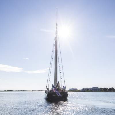 a sailboat out in the open waters with a barrier island in the background
