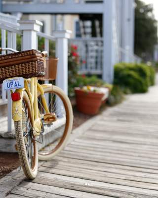 A yellow bike resting on its stand adjacent to white railing on a porch on a waterfront boardwalk.