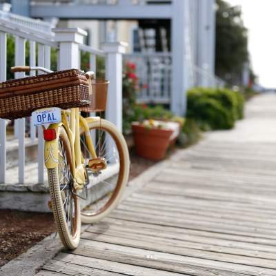 A yellow bike resting on its stand adjacent to white railing on a porch on a waterfront boardwalk.