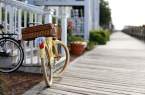 A yellow bike resting on its stand adjacent to white railing on a porch on a waterfront boardwalk.