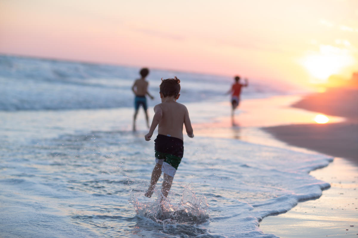 Boys running along the shore at sunset