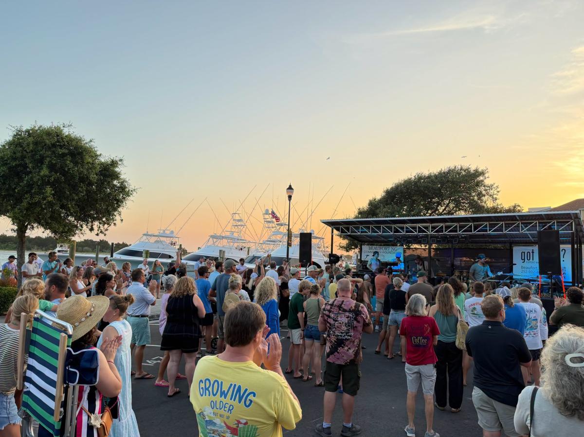 Group of people enjoying live music by the water with the sun setting in the background