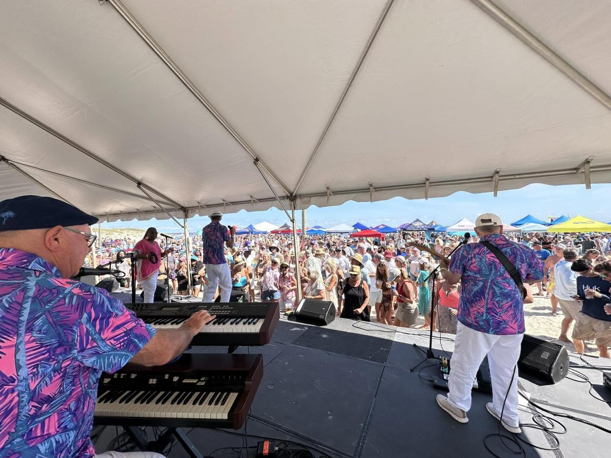 Band playing on a stage with fans standing on the beach enjoying the music