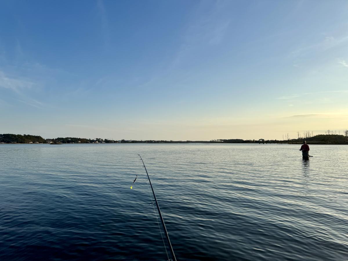 two people wading in the water fishing at sunset
