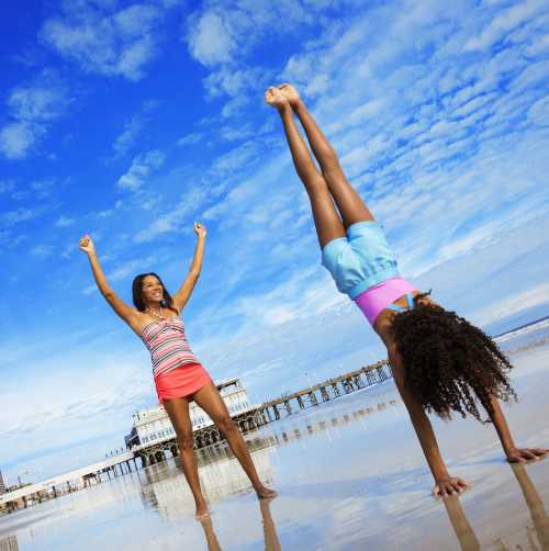 A child doing a handstand on the beach while her mom cheers her on