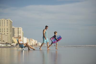 A family enjoys a sunny day on the shoreline with hotels in the background.