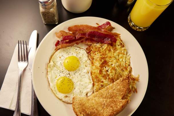 Table placed with a plate full of eggs, toast, bacon, hashbrowns, coffee, and orange juice