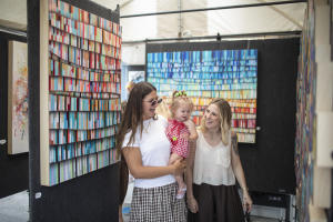 Two women holding a small child smiling and looking at art.