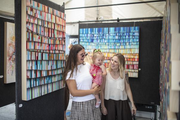 Two women holding a small child smiling and looking at art.