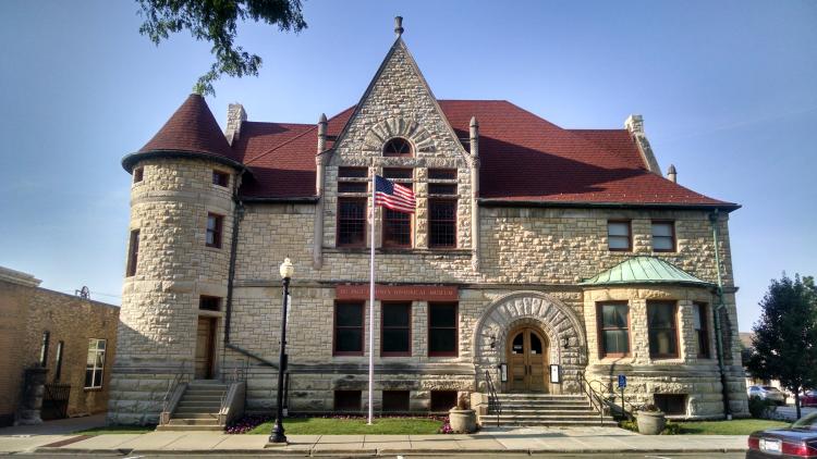 Exterior of the DuPage County Historical Museum, a historic limestone building with a red roof and an American flag in front.