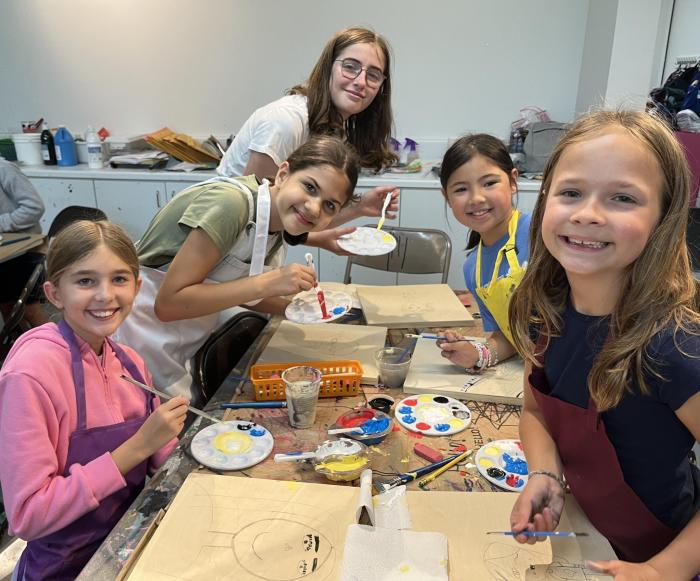 there are five young girls sitting around a table painting. They are all happy to be there.