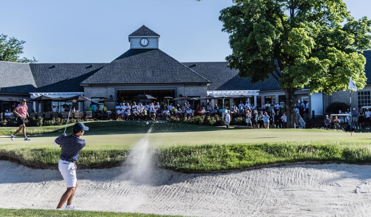 Young golfer teeing off near clubhouse with crowd watching