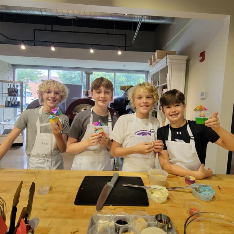 four tween boys making and decorating cupcakes. two are blonde, two are brunette.
