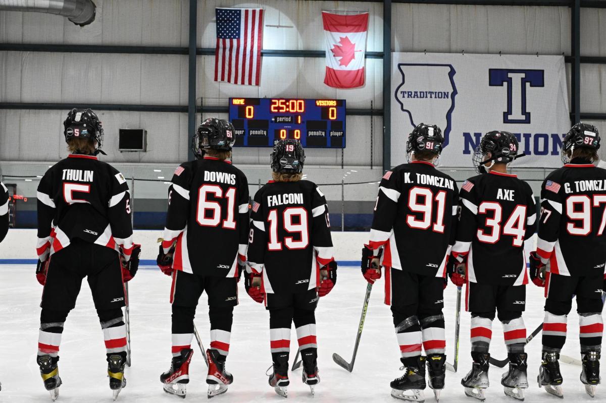 Youth hockey players on the ice facing country flags during National Anthem