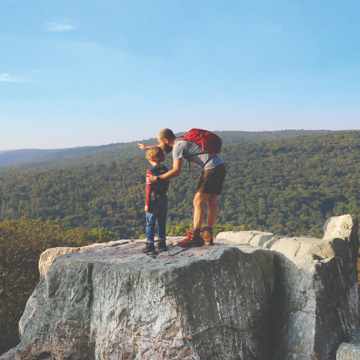 Man and child with backpacks overlook scenic view at Chimney Rock.