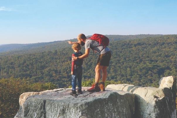 Man and child with backpacks overlook scenic view at Chimney Rock.