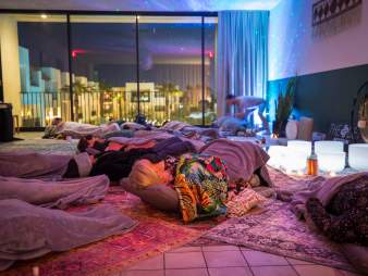 A serene Sound Bath meditation space with attendees resting on mats under soft lighting, surrounded by blankets and soothing crystal bowls.
