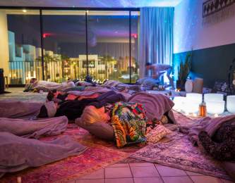 A serene Sound Bath meditation space with attendees resting on mats under soft lighting, surrounded by blankets and soothing crystal bowls.