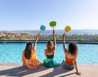 Three girl friends holding up fans and posing for a photo poolside at The Ritz-Carlton, Rancho Mirage.