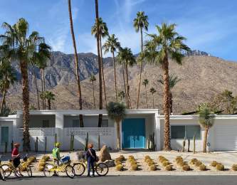 People are on their bike in front of a home in Palm Springs with the mountains in the background.