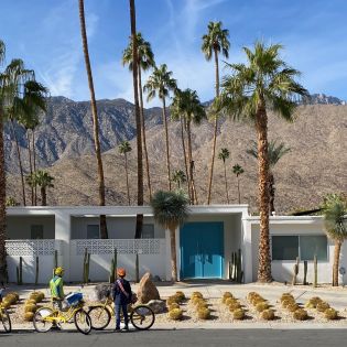 People are on their bike in front of a home in Palm Springs with the mountains in the background.