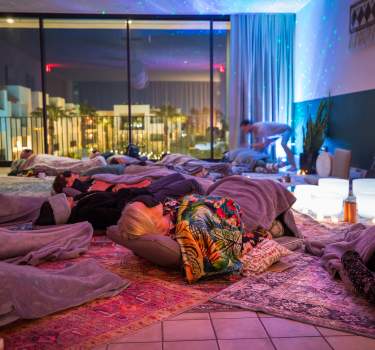 A serene Sound Bath meditation space with attendees resting on mats under soft lighting, surrounded by blankets and soothing crystal bowls.