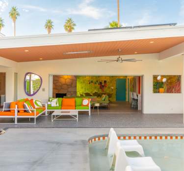 Palm Springs Vacation Rental modern patio with colorful seating, a pool, and a bright interior view featuring vibrant decor.