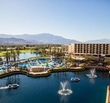 Aerial view of lake by resort and mountains in background with blue sky